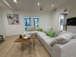 A modern living room with a grey sectional sofa, a wooden coffee table, and pendant lights. - 2 Bed - Sleeps 5 - Garden - Hot-tub (London)