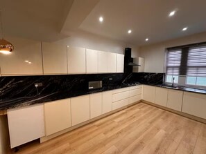 A modern kitchen with white cabinets, black countertops, and a wooden floor. - 2 Bed - Sleeps 5 - Garden - Hot-tub (London)