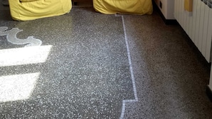 Una habitación con dos sofás amarillos, una pequeña mesita de madera con una lámpara, un radiador y una ventana con cortinas.