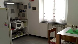 A kitchen with a refrigerator, microwave, and stove, a dining table with chairs, a window with curtains, and a clock on the wall. - Charming 2-bedroom Apartment in the Heart of Genova (Genoa)