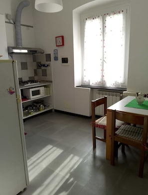 Une cuisine équipée d’un réfrigérateur, d’un four à micro-ondes et d’une cuisinière, une table à manger avec des chaises, une fenêtre avec des rideaux et une horloge au mur.