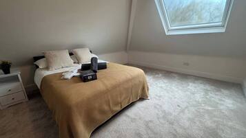 A bedroom with a bed, pillows, a bedside table, a small plant, a window, and a carpeted floor.