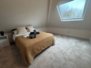 Een slaapkamer met een bed, kussens, een nachtkastje, een klein plantje, een raam en een vloerbedekking.