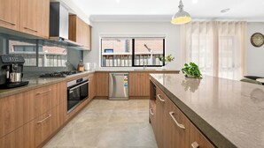 A modern kitchen with wooden cabinets, a stainless steel refrigerator, a built-in oven, and a large window with curtains. - Park-fronted Luxury Grand Family House with Gym, Heated Pool/Spa, Tennis Court. (Mambourin)