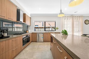 Eine moderne Küche mit Holzschränken, einem Edelstahlkühlschrank, einem eingebauten Backofen und einem großen Fenster mit Vorhängen.