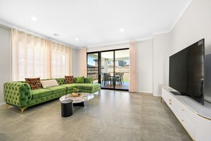 Uma sala de estar moderna com um sofá verde, uma televisão de tela plana e uma porta de vidro deslizante que dá para uma área externa.