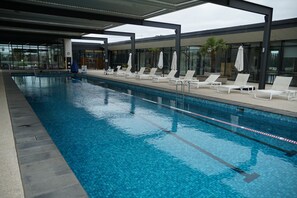 A swimming pool with lounge chairs and umbrellas, surrounded by a modern building with large windows. - Park-fronted Luxury Grand Family House with Gym, Heated Pool/Spa, Tennis Court. (Mambourin)