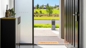 An interior space with a sliding door leading to an outdoor area, a cabinet with decorative items, and a welcome mat. - Park-fronted Luxury Grand Family House with Gym, Heated Pool/Spa, Tennis Court. (Mambourin)