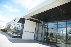 A modern building with large glass windows and a sign that reads 'CLUB MAMBOURIN'. - Park-fronted Luxury Grand Family House with Gym, Heated Pool/Spa, Tennis Court. (Mambourin)