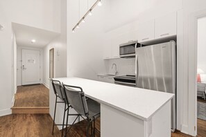 A modern kitchen with a white countertop, stainless steel appliances, and a bar stool. - Penthouse 2BR Montreal Loft • Walk to Old Port (Montreal)