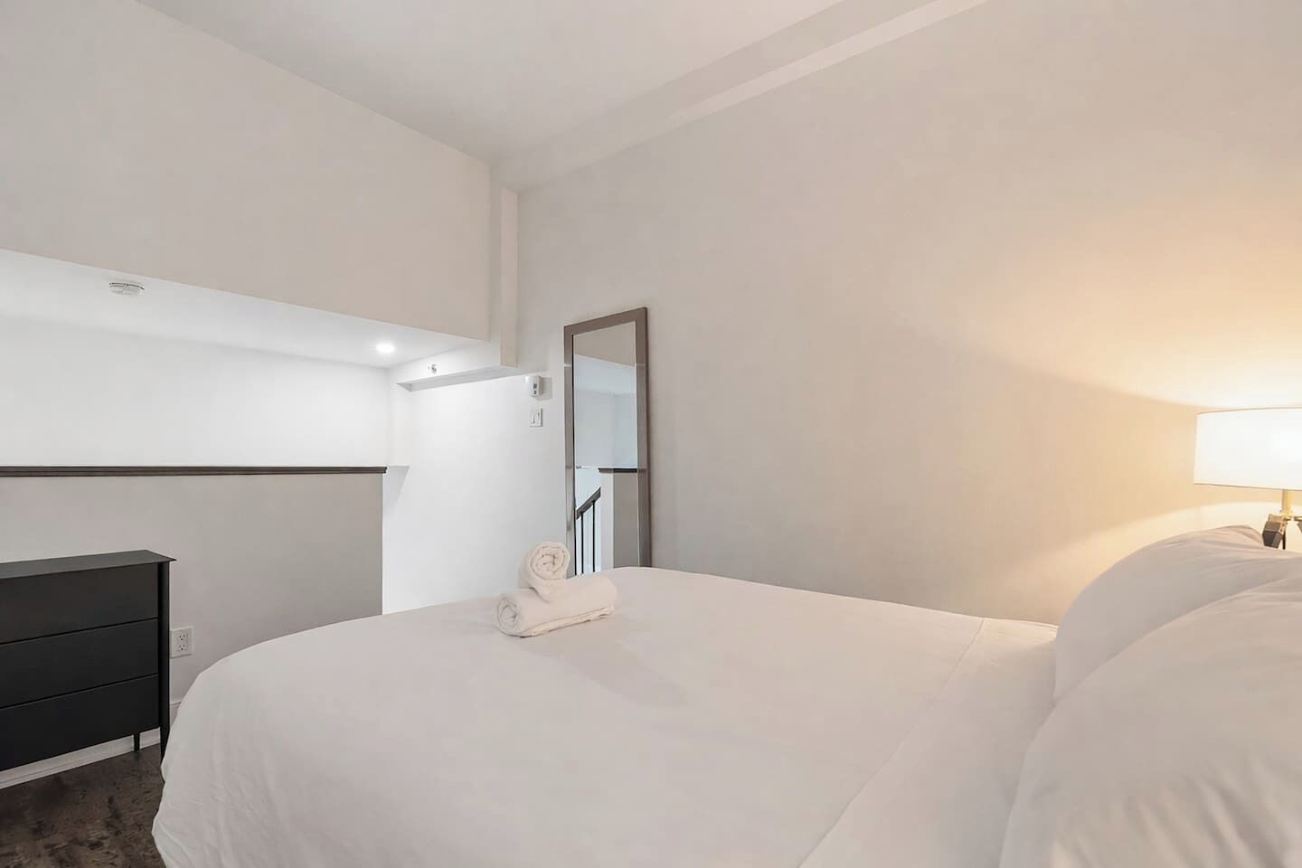Ett hotellrum med en säng, en byrå, en spegel och en lampa.