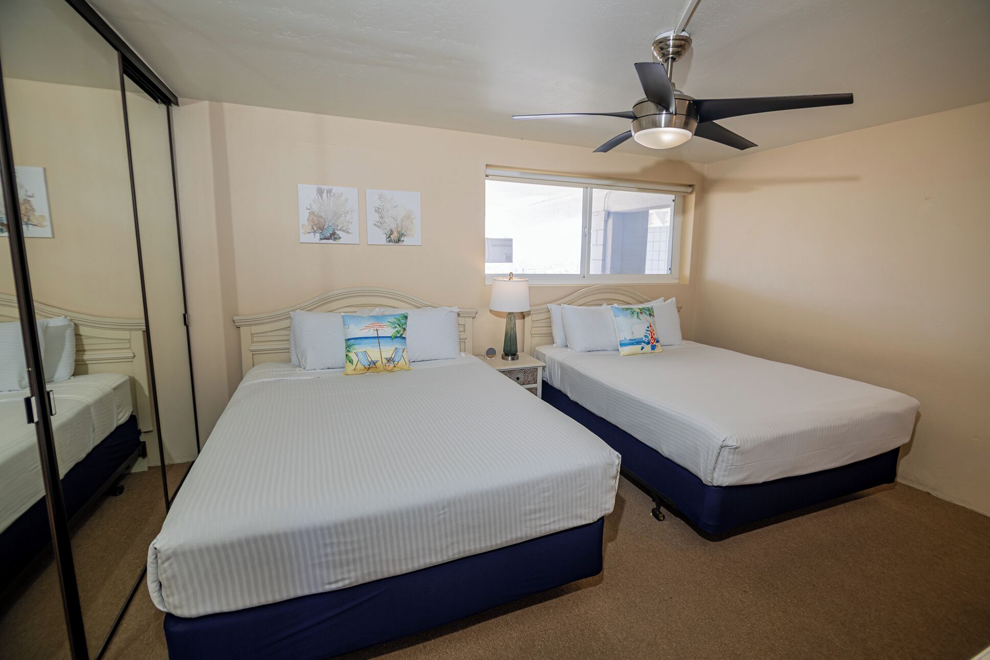 A bedroom with two beds, a ceiling fan, a window, and artwork on the wall.