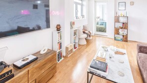 Uma sala de estar moderna com uma televisão de tela plana grande, móveis de madeira, uma mesa de centro com livros e uma estante.