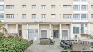 Um edifício de vários andares com uma placa na entrada que diz 'ESSEX PLACE'. Há bancos e um canteiro de flores na frente.