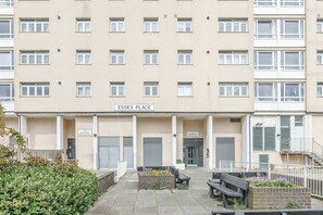 Ein mehrgeschossiges Gebäude mit einem Schild, auf dem 'ESSEX PLACE' steht. Vor dem Eingang befinden sich Bänke und ein Blumenbeet.
