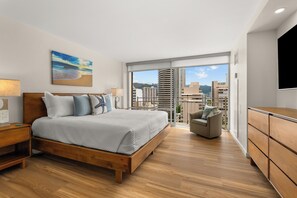 A modern bedroom with a large bed, a nightstand, a dresser, and a view of the city through large windows. - 14th Floor Waikiki City & Mountain Views! Full Kitchen! Walk to Beach! (Honolulu)