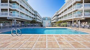 Piscina com plataforma de mergulho, rodeada por espreguiçadeiras e um edifício com varandas.