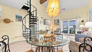 A dining area with a glass table, chairs, and a spiral staircase. - 2BR with loft, sleeps 8, lagoon front, pool & private beach access (Gulf Shores)
