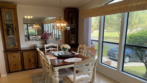 Uma sala de jantar com mesa de madeira, cadeiras brancas, um candelabro e vista para o exterior.