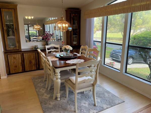 A dining area with a wooden table, white chairs, a chandelier, and a view of the outdoors.