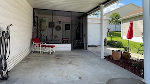 Varanda coberta com piso de concreto, um guarda-sol vermelho e uma cadeira branca.