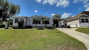 Uma casa de dois andares com varanda frontal coberta, garagem e gramado bem cuidado.