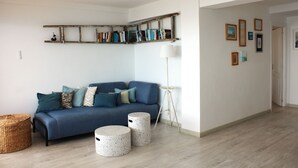 A living room with a blue sofa, two round stools, a floor lamp, and a bookshelf. - Your Mediterranean dream home  - Costapinosmar (Salou)