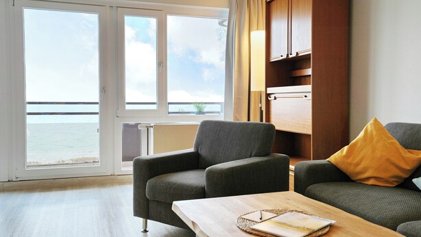 Ein Zimmer mit einer Couch, einem Tisch und Meerblick durch große Fenster.
