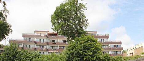 Ein mehrstöckiges Gebäude mit Balkonen, umgeben von Bäumen und blauem Himmel.