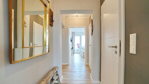 Un pasillo con un banco de madera, un espejo grande y una puerta que da a otra habitación.