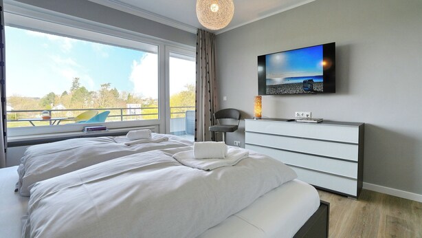 Un dormitorio moderno con una cama grande, un televisor de pantalla plana, una mesita de noche y vistas al exterior.