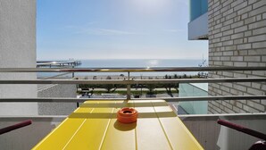 Un balcón con una mesa amarilla, un muro de ladrillo y vista al mar y un muelle.
