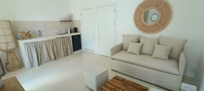 Un espace de vie minimaliste comprenant un canapé, un pouf et un miroir rond accroché au mur.