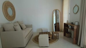 A living room with a sofa, a coffee table, a small table, a mirror, a wooden shelf, and a window with curtains. - La Maison Coloniale II (Grand Baie)