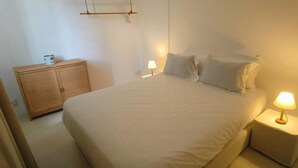A bedroom with a bed, bedside lamps, a wooden cabinet, and a hanging light fixture. - La Maison Coloniale II (Grand Baie)