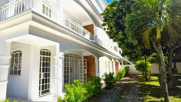 A white building with multiple windows, a balcony, and a pathway with greenery. - La Maison Coloniale II (Grand Baie)