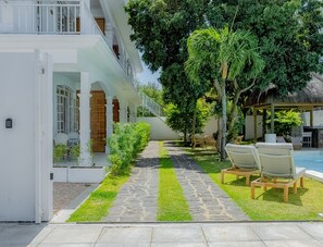 Ein Hotel mit einem gepflasterten Weg, der zu einem Poolbereich führt, umgeben von Grünpflanzen und Sitzgelegenheiten im Freien.
