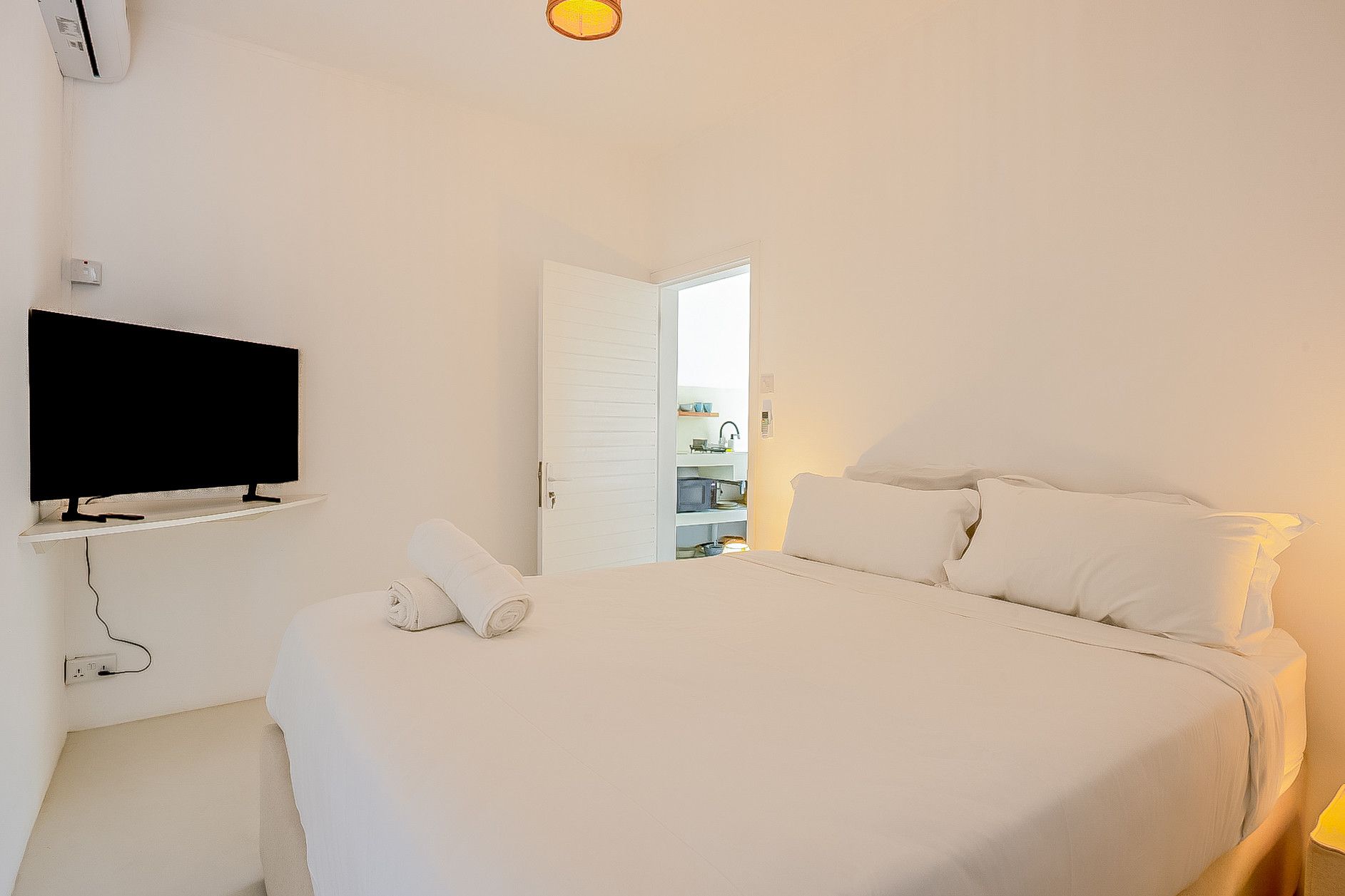 A hotel room with a bed, a flat-screen TV mounted on the wall, and a door leading to a bathroom.