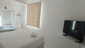 Een hotelkamer met een bed, een televisie, een spiegel, een raam en een kledingkast.