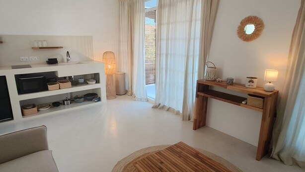 Een moderne keuken met inbouwapparatuur, een eethoek met een houten tafel en een groot raam met gordijnen.