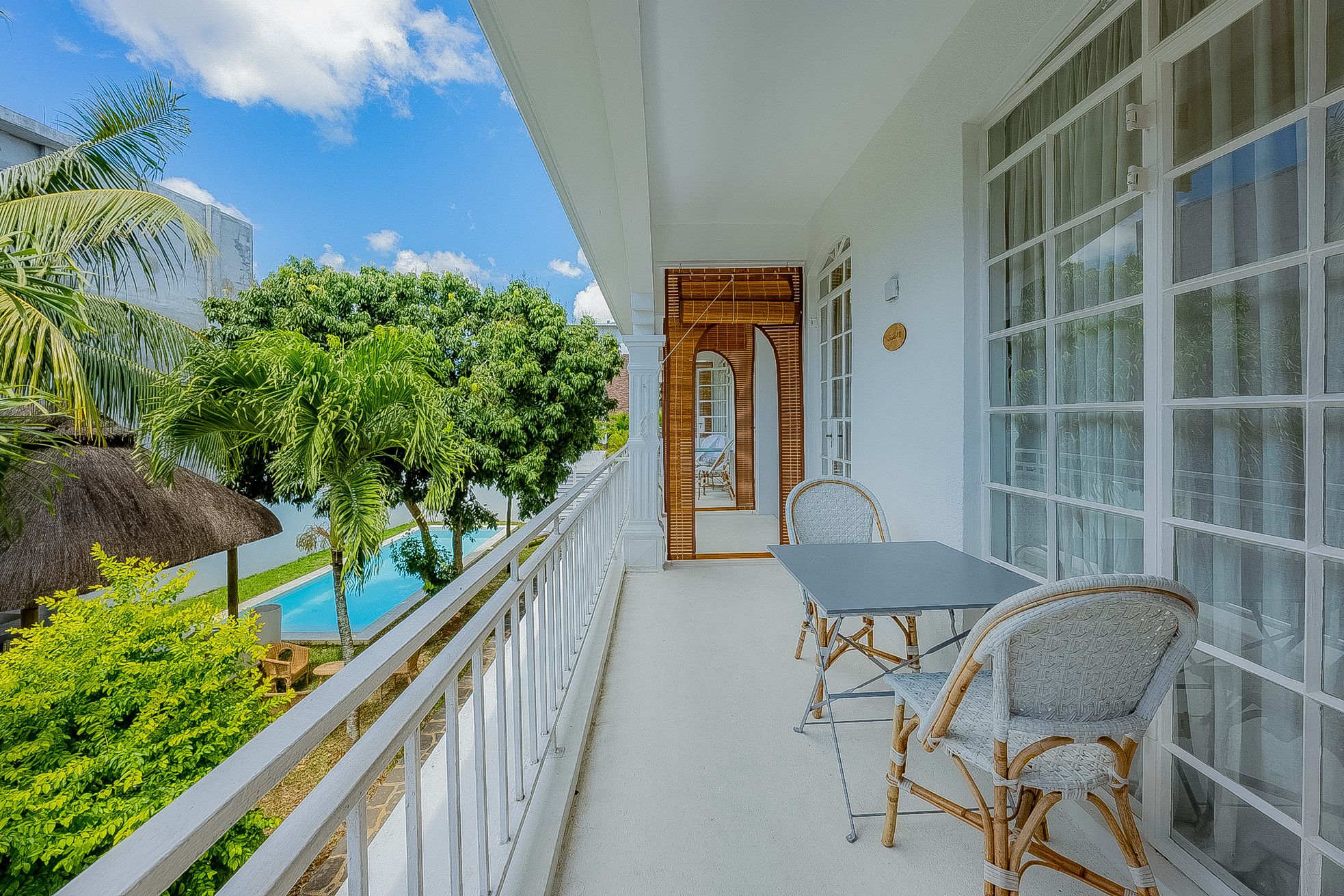 Ein Balkon mit Tisch und Stühlen, Blick auf ein Schwimmbecken und üppiges Grün.