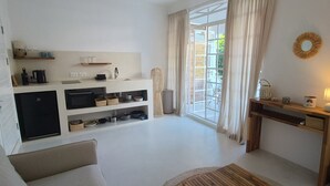 Een ruimtelijke woonruimte met kitchenette, een bank, een eettafel en een groot raam met gordijnen.
