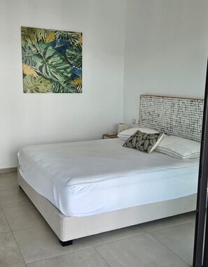 A bedroom with a bed, a headboard, a nightstand, a pillow, and a wall-mounted painting.