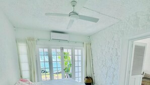 A bedroom with a bed, a ceiling fan, a window with curtains, and a door with shutters. - Villa Anse Turquoise - Breathtaking sea view (Anse La Raie)