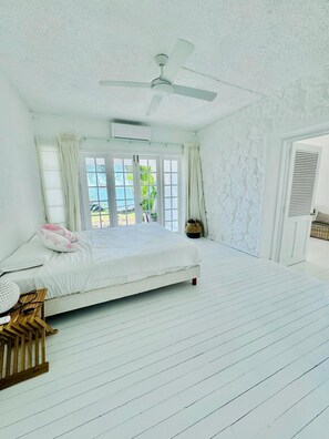 Ein Schlafzimmer mit einem Bett, einem Deckenventilator, einem Fenster mit Vorhängen und einer Tür mit Fensterläden.