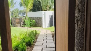Una entrada de edificio moderno con un camino de hormigón que lleva a una estructura blanca, rodeada de vegetación y un cielo despejado.