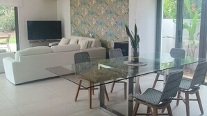 Ett modernt vardagsrum med ett matbord i glas, en vit soffa och en platt-TV.