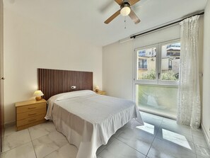 A bedroom with a bed, a nightstand, a ceiling fan, a window with a view, and a door. - Spacious apartment, sea view - 4 guests (Roses)