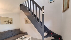 Una escalera con barandilla negra y detalles rojos, un sofá gris, una mesa de centro blanca y dos obras de arte enmarcadas en la pared.