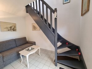 A staircase with a black handrail and red accents, a gray sofa, a white coffee table, and two framed artworks on the wall. - House near the beach, pets welcome - 4 guests (Sarzeau)